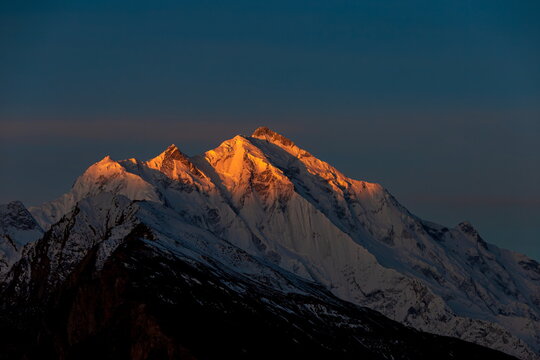 View of the sun-kissed, snow-capped mountain peaks pierce the twilight sky, a stunning contrast of light and shadow, Hunza, Gilgit Baltistan, Pakistan.