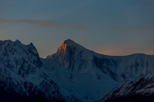 View of snow-capped peaks kissed by the warm glow of the setting sun, casting long shadows across the mountainous terrain, Hunza, Gilgit Baltistan, Pakistan.