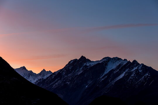 View of jagged, snow-dusted peaks pierce the twilight sky, a dance of orange and blue painting the horizon in Hunza, Gilgit Baltistan, Pakistan.