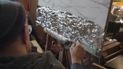 Senior artist on a wheelchair applies silver to the oil painting