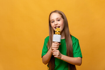 Happy pretty little girl in green t-shirt holding the microphone in her hands on yellow background. Child sings a song, speaks into a microphone, hosts a TV show, performs on the radio