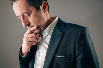 Pensive businessman in suit reflecting on a difficult choice, representing hesitation, analysis, risk assessment, stress, or strategic thinking.
