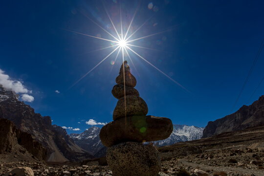 View of a carefully balanced stone cairn stands defiantly against the stark, blue sky, sunburst high above, Karakoram Highway, Passu, Gilgit Baltistan, Pakistan.