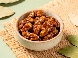 Obraz premium Delicious candied walnuts in a small ceramic bowl on burlap with bay leaves on a light green surface
