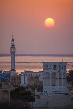 Aerial view of a minaret piercing the dusky sky as the sun sets behind the cityscape, casting a warm glow over the water, Isfahan, Isfahan Province, Iran.