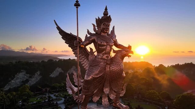 A golden, winged statue of a deity riding a bird, silhouetted against a sunrise