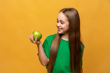 Happy smiling little girl in green t-shirt holding green apple isolated on yellow background. Proper nutrition. Child health. vegetarianism. High quality photo. Copy space