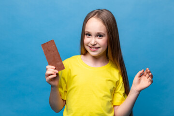 Cute little girl in yellow casual t-shirt holds chocolate bars on blue background, closeup. The concept of children's happiness and love for sweets. High quality photo. Copy space