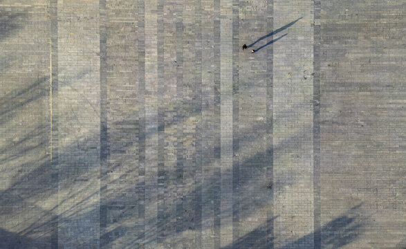 Aerial view of shadows stretching across a patterned stone ground, with two figures casting long silhouettes, Pingyao, Jinzhong, Shanxi, China.