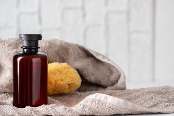 Amber shampoo bottle and a yellow sea sponge resting on a tan towel, with a blurred white brick wall of the bathroom in the background.
