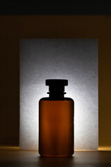 A bottle with a dark liquid is silhouetted in the center, with a backlit white card behind it, creating a dramatic, high-contrast image.