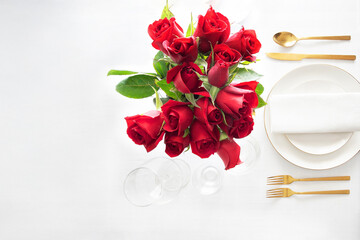 A beautiful place setting for a romantic dinner, featuring a bouquet of red roses, gold cutlery, and a plate with a clean napkin, all on a bright white background.