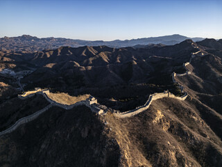 Aerial view of The Great Wall snaking across rugged, mountainous terrain under a crisp, clear sky, a testament to ancient engineering and enduring beauty, Jingshanling, Beijing, China.