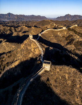 Aerial view of the serpentine Great Wall, a dragon's spine snaking across rugged mountains under a crisp blue sky, Jingshanling, Beijing, China.