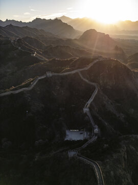 Aerial view of the snaking Great Wall of China, a stone dragon winding through the rugged mountains under the glow of the setting sun, Jingshanling, Beijing, China.