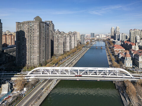Aerial view of a vibrant cityscape where modern buildings meet the tranquil Hai River, dissected by a prominent white bridge, Tianjin, Tianjin, China.