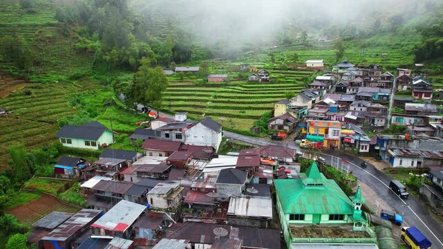 Aerial close up drone footage of a village in the high plateau volcanic mountains of Dieng in Indonesia, under a fogy atmosphere