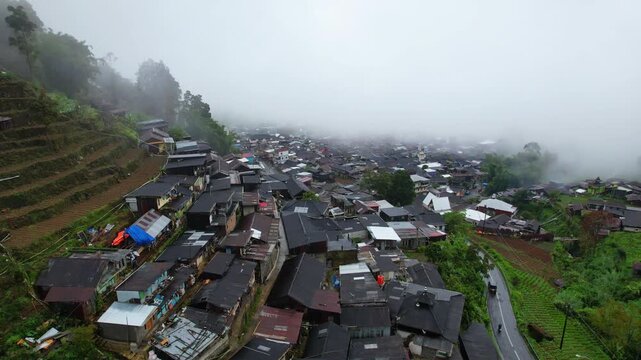 Aerial drone footage of a local village in the high plateau, volcanic mountain area of Dieng in Indonesia, under an extreme heavy fogy atmosphere