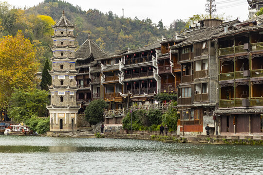 View of ancient architecture reflected in the tranquil river waters, with vibrant autumn foliage adding a splash of color, Fenghuang Ancient Town, Hunan, China.