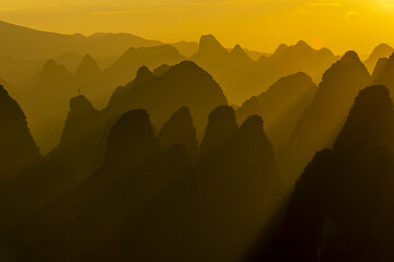 View of golden light washes over the karst mountains, creating a dreamlike landscape with soft shadows and a serene atmosphere, Xingping, Guillin, China.