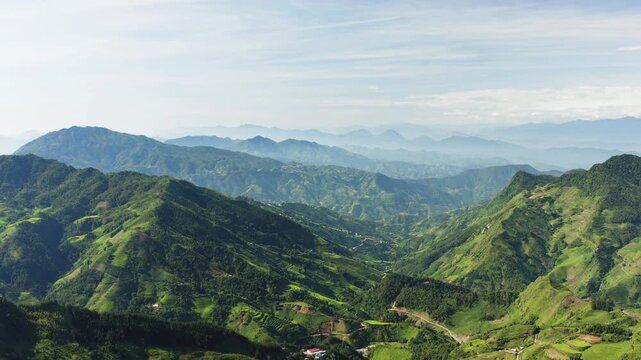 Cinematic tracking footage of the northern Vietnamese mountains. Featuring vibrant green terraces, remote valley settlements, and misty blue peaks under a bright highland sky.