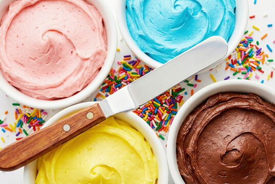 Colorful bowls of vibrant frosting and sprinkles with an offset spatula, perfect for baking and decorating cakes or cupcakes.