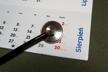 Handwritten text 'Sierpień' on a calendar displayed alongside a stethoscope. The calendar highlights dates for medical appointments, suggesting healthcare planning.