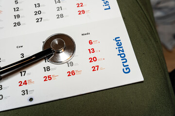 A close-up of a calendar page for December featuring dates highlighted in red, accompanied by a stethoscope, symbolizing the healthcare profession and time management in medical practice.