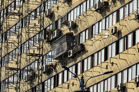 View of a beige building facade adorned with repeating geometric patterns, windows, and numerous air conditioning units under the sun, Chongqing, Chongqing, China.
