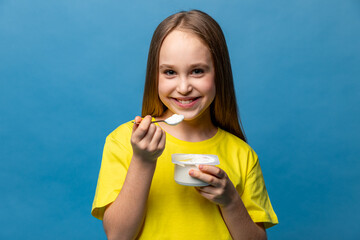 Cute little girl in yellow t-shirt eating tasty yogurt on light blue background. Healthy nutrition concept. Copy space. High quality photo
