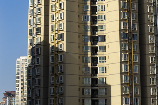 View of sunlight casting shadows on the facade of a high-rise residential building with white window frames against a clear blue sky, Xi'An, Shaanxi, China.