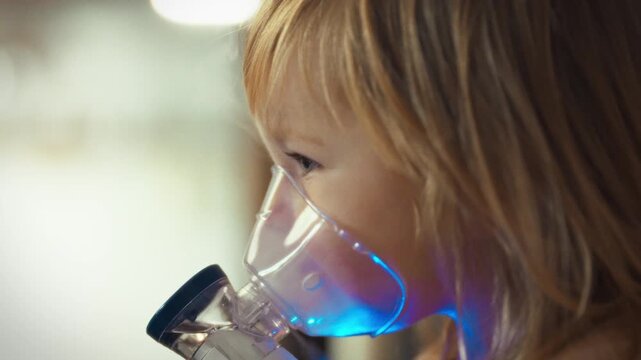 Young child's tiny hands carefully hold nebulizer device, undergoing vital inhalation treatment in a medical setting. The child is undergoing a crucial health procedure to alleviate respiratory issues