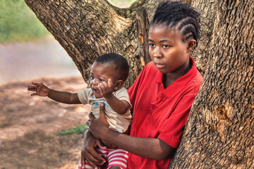 family village african mother holding baby, dreadlocks braids hairstyle, outdoors in the nature , near a tree