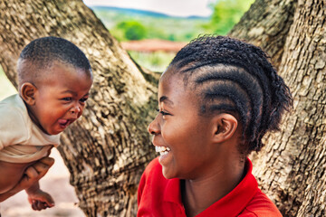 family village african mother playing with baby, dreadlocks braids hairstyle, outdoors in the nature , near a tree