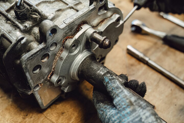 Disassembled old car gearbox with gears and tools on a workbench in an auto service garage. Repair, maintenance, and replacement of worn mechanical transmission parts in a vehicle.
