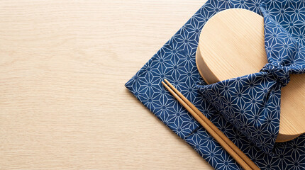 Minimal Japanese furoshiki lunch box - bento, scene with blue patterned cloth and chopsticks on light wood table. For bento branding, packaging design. Top view, copy space.