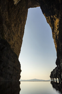 View of a reflective pool mirroring the sky through a towering stone archway, creating a serene contrast of textures and light, Zhangjiajie, Hunan, China.