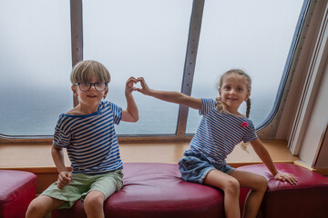 Two kids on summer trip at a boat form heart with their arms