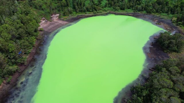 Aerial drone footage of a sulfuric opal color lake in Dieng Plateau, a high altitude volcanic mountain area in Indonesia, with forest around