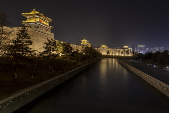 View of the ancient city wall illuminated in golden light, reflecting in the tranquil water, a blend of history and modernity in Datong, Shanxi, China.