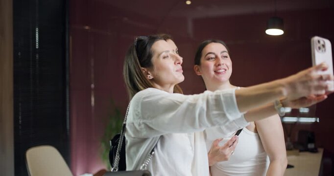 Three women are engaged with their smartphones, sharing a light-hearted moment together in a contemporary space during a sunny day. Their joy and connection are evident