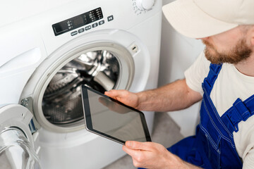 Repairing a washing machine at home by a technician with a tablet in hand