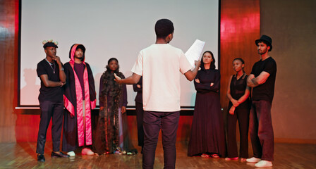 African young adult gen z male man hold scripts paper read play story lines scene standing indoor stage hall. Happy group boy girl clap hand enjoy do work show drama practice day inside campus place