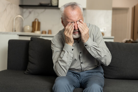 Man struggles with tired eyes and blurred vision while sitting on a couch at home