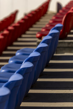View of rhythmic rows of vibrant blue and red stadium seats cast stark shadows on sun-drenched concrete steps, creating a captivating visual harmony, Beijin, Beijin, China.
