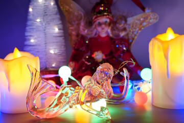 A toy mermaid and a fairy on the background of a glowing Christmas tree garland and decorative candles.