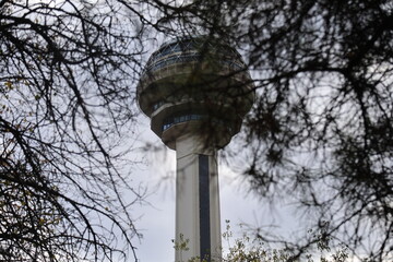Peaceful autumn landscape in Botanik Park, Ankara, featuring the iconic Atakule tower, colorful fall foliage, empty wooden benches, a scenic pond with fountains, and calm nature city views.
