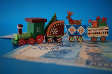 A toy Christmas train and paper bills on a blue background.