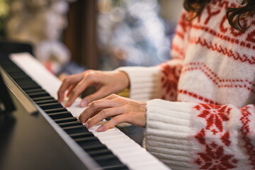 Obraz premium Close-up of a professional female pianist's hands, wearing a red and white Christmas pattern knitted sweater, playing classical music on the black and white keys of a piano with bokeh background