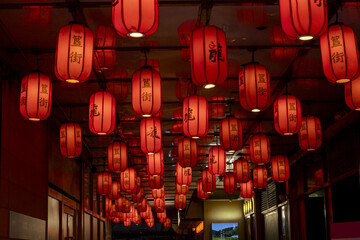 View of vibrant red lanterns with bold black characters illuminate a narrow passage, casting a warm glow on the dark walls in Beijing, Beijing, China.